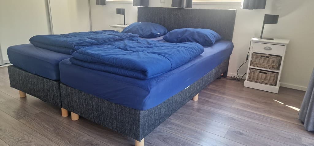 Slaapkamer met een dubbel bed met blauwe dekbedden en een nachtkastje naast het bed.