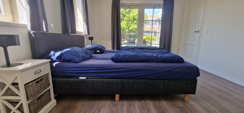 Slaapkamer met een tweepersoonsbed, nachtkastje en grote ramen die uitzicht geven op de buitenruimte.