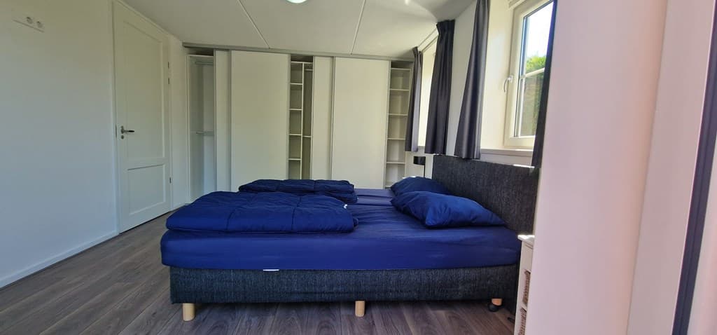 Slaapkamer met twee aparte bedden en een kledingkast, voorzien van grote ramen voor natuurlijk licht