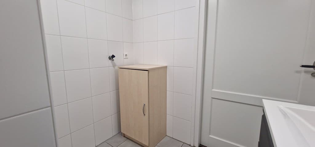 Witte betegelde hoek met een houten kast en een wastafel in een badkamer