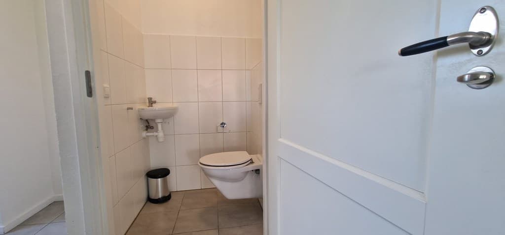 Kleine toiletruimte met toilet en wastafel, betegelde wanden en een vloer van tegels.