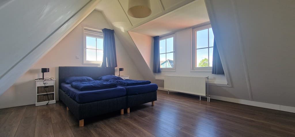 Slaapkamer met twee bedden, grote ramen en houten vloer, gelegen onder een schuin dak met zicht op de buitenlucht