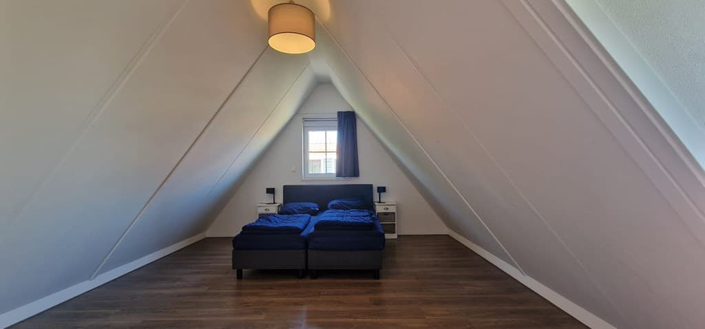 Sfeervolle zolderkamer met schuin oplopende wanden, bed met blauwe dekbedden en nachtkastjes aan beide zijden