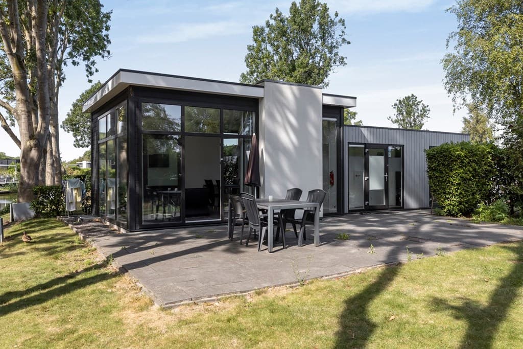 Moderne vakantiewoning met glazen gevel en terras, omgeven door groen en bomen.