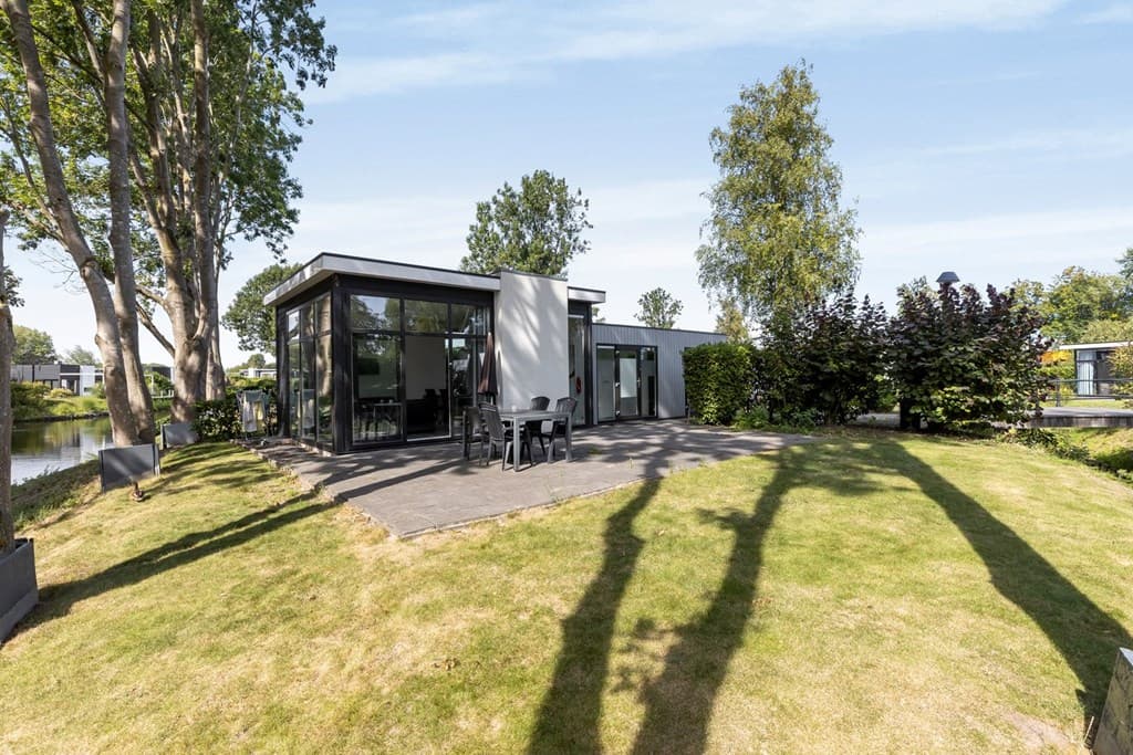 Moderne vakantiewoning met grote ramen, omringd door groen en een bestrate buitenruimte aan het water