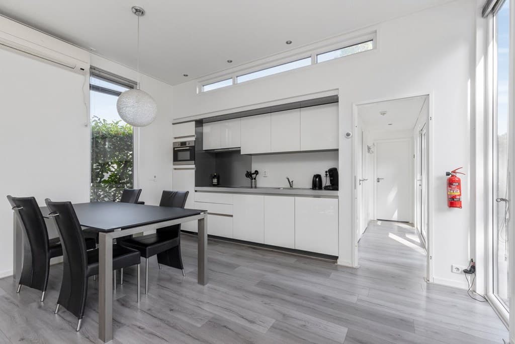 Moderne open keuken met eettafel en zwarte stoelen, veel lichte ruimte door grote ramen.