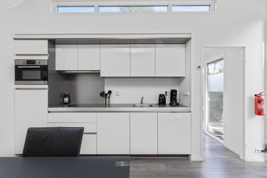 Moderne, lichte keuken met witte kastjes, een kookplaat en een deur naar buiten.