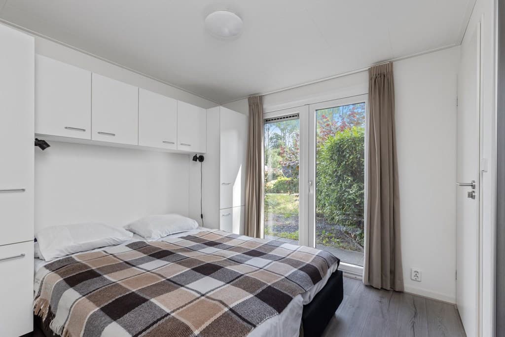 Slaapkamer met een tweepersoonsbed, kledingkasten en toegang tot een tuin met groene omgeving.