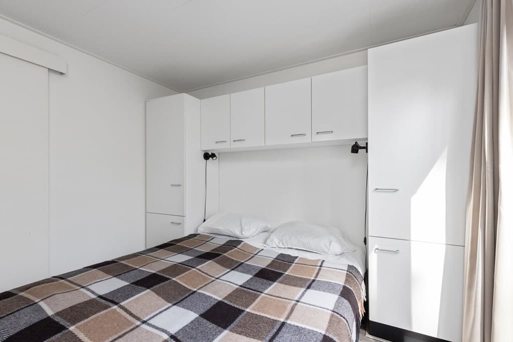 Slaapkamer met een dubbelbed, witte kastenwand en een geblokte dekens.