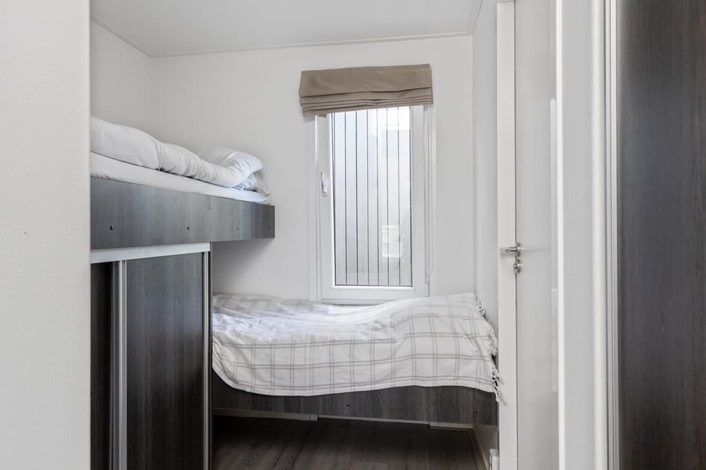 Slaapkamer met stapelbed en raam met jaloezieën, eenvoudige inrichting en lichte muren.