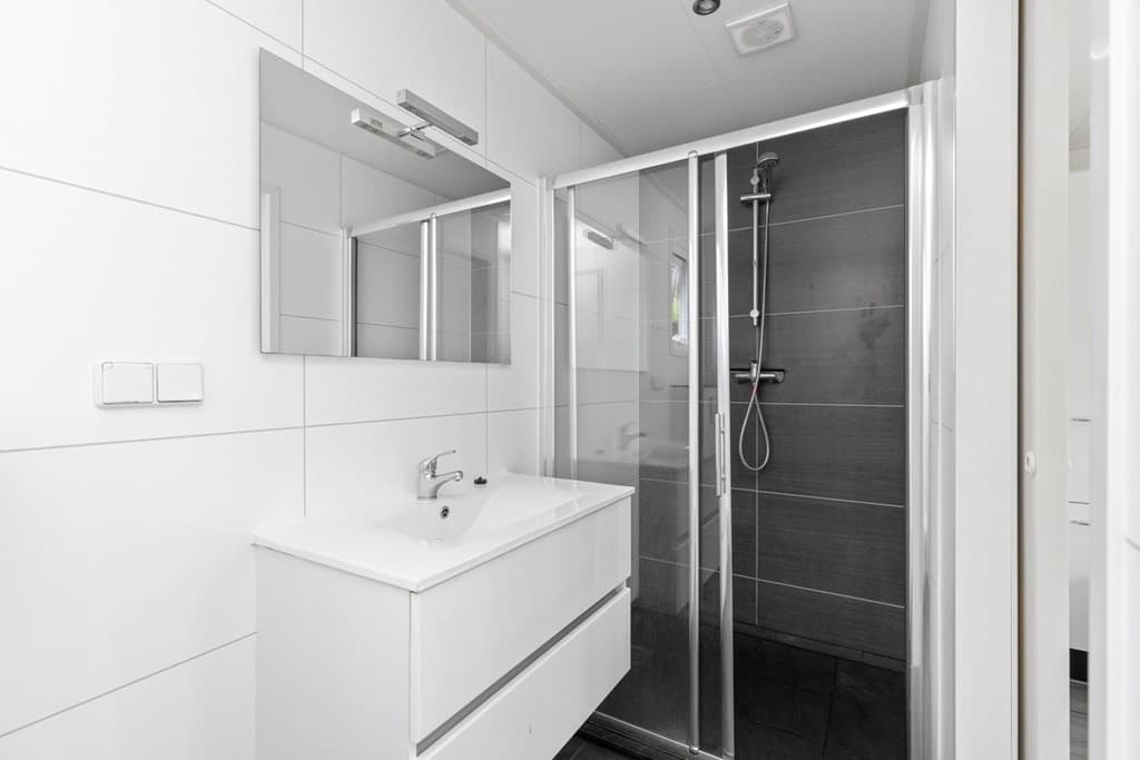 Moderne badkamer met inloopdouche, wastafel met spiegel en lichte wand- en vloerafwerking.