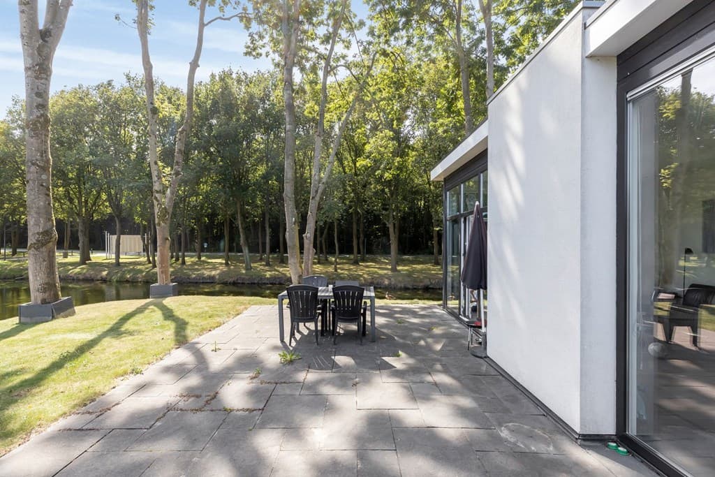 Terras met een eettafel en stoelen, omringd door bomen en uitzicht op een waterpartij