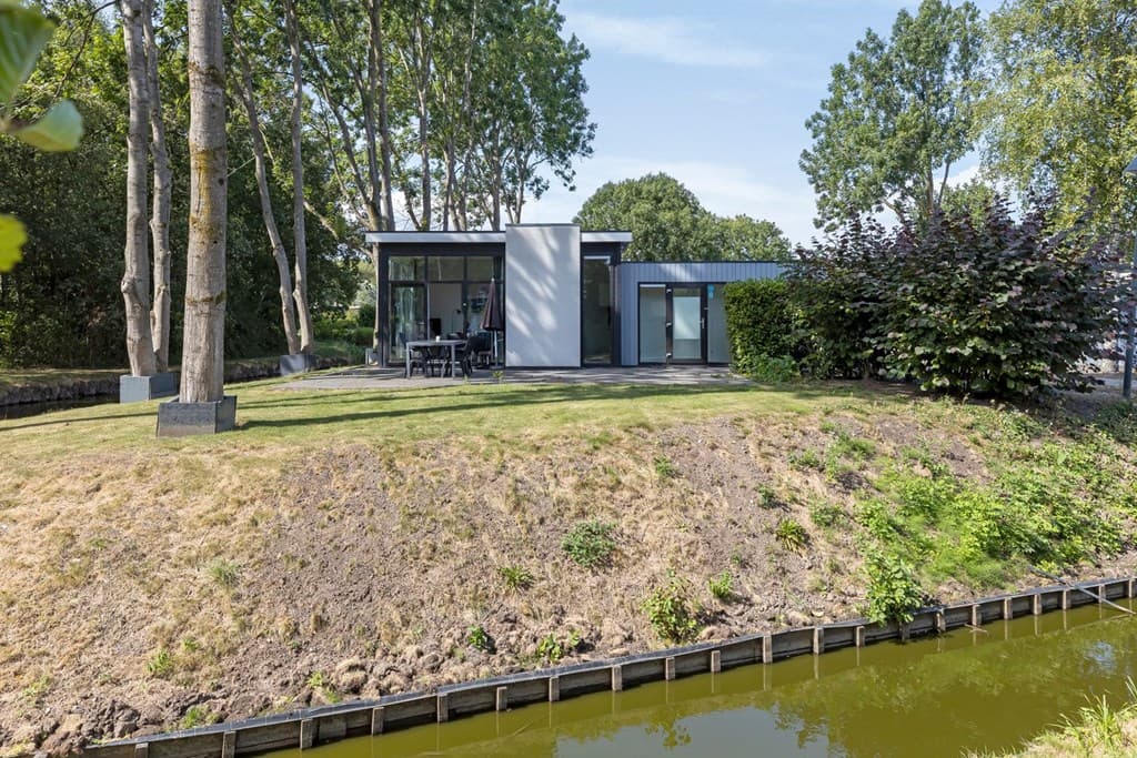 Moderne woning met grote ramen, omringd door bomen en een grasveld, gelegen aan een waterpartij in EuroParcs Spaarnwoude.