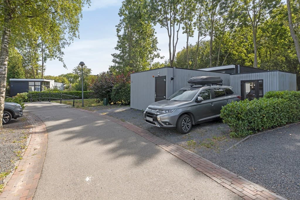 Moderne vakantiewoning met grijs exterieur, gelegen aan een asfaltpad omringd door groen en bomen.