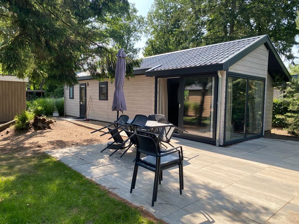 Vakantiehuis met een terras, stoelen, parasol en grote ramen, omgeven door groen op EuroParcs Zuiderzee