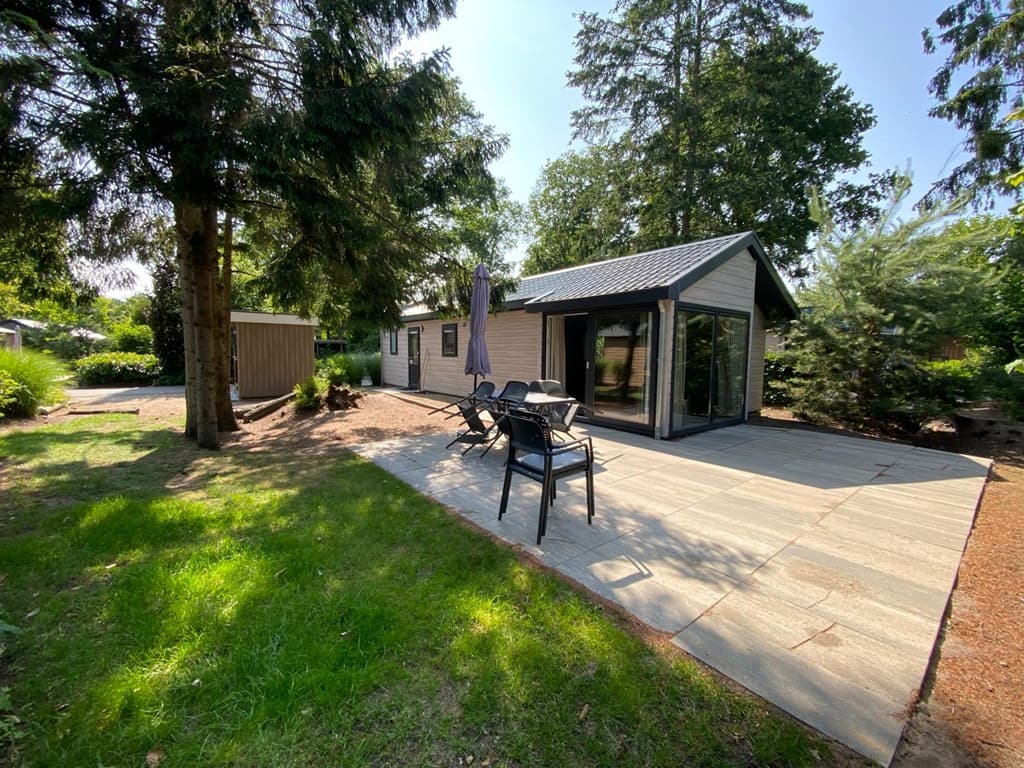Moderne bungalow met terras, tuinstoelen en zicht op groene omgeving met bomen en struiken.