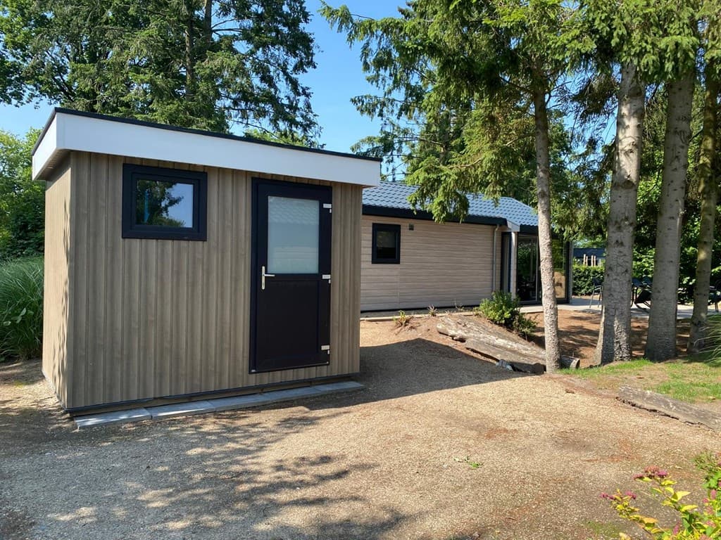 Twee vakantiewoningen omringd door bomen, met een grindpad en gras in EuroParcs Zuiderzee, Biddinghuizen.