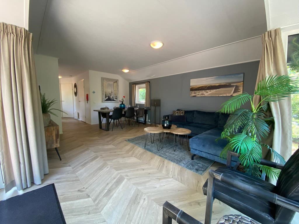 Lichte woonkamer met zithoek, eettafel en decoratieve planten, uitgevoerd in warme tinten en houten vloerdelen