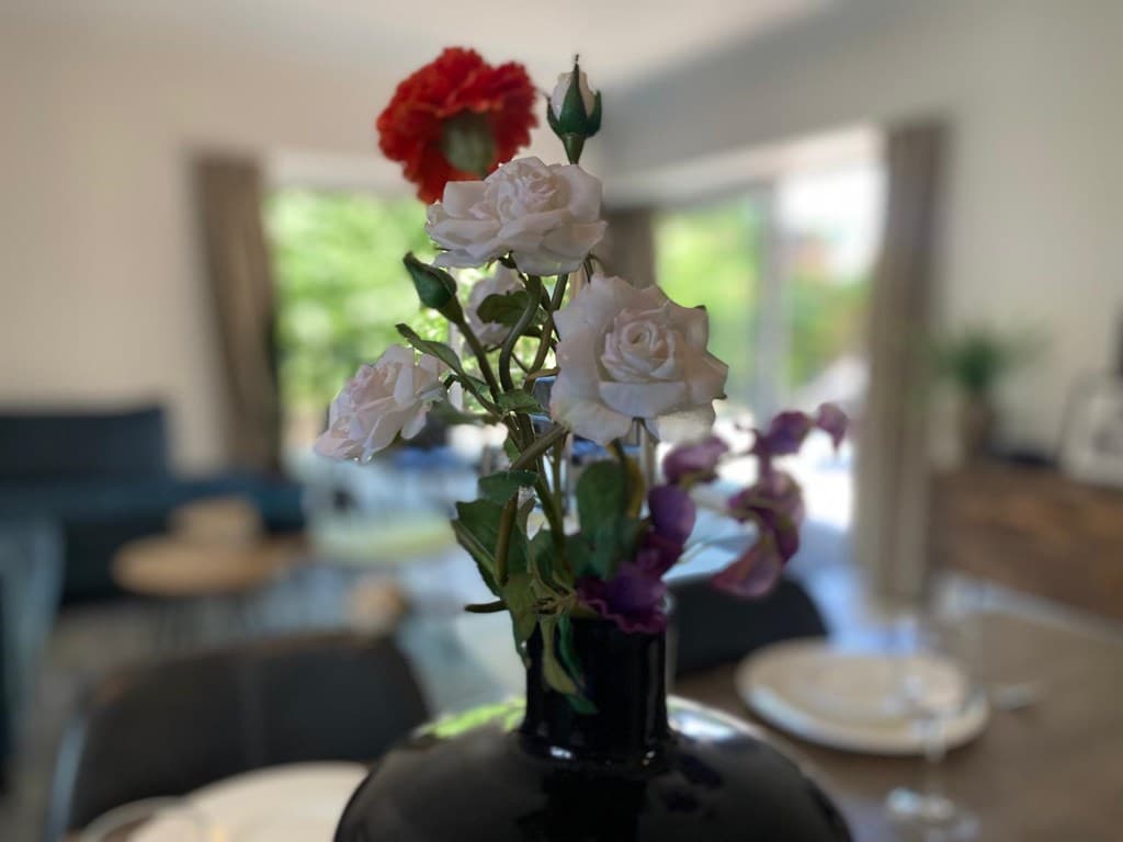 Vaas met bloemen in een interieur met een bank en een eettafel zichtbaar op de achtergrond.