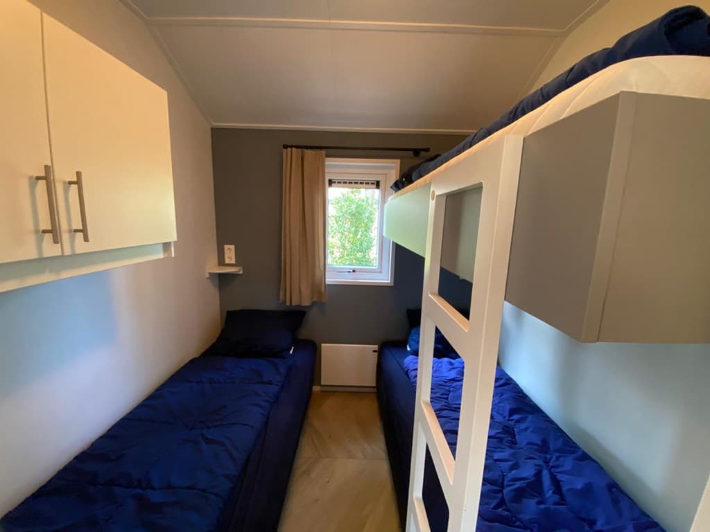 Slaapkamer met twee aparte bedden en een stapelbed, muurkast en raam met uitzicht op groen.