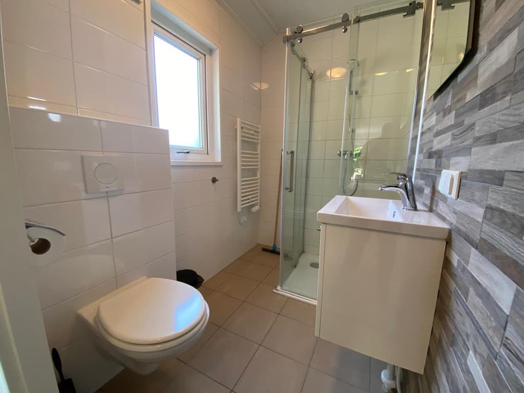 Moderne badkamer met douche, toilet, wastafel en een raam voor natuurlijke lichtinval.