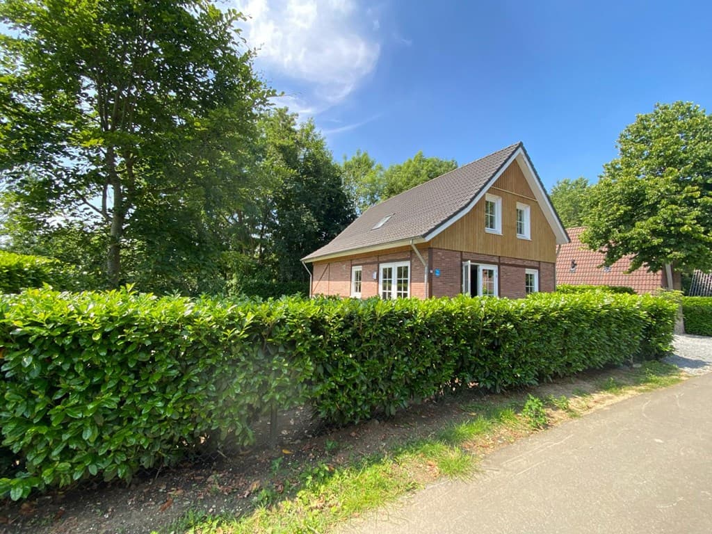 Woning met een houten gevel en puntdak, omgeven door groen en een oprit met grind aan de voorzijde.