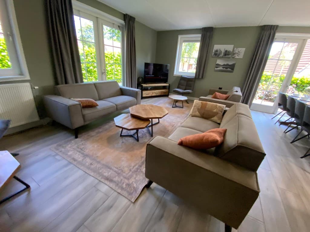 Zitkamerruimte met twee banken, salontafel, tv en ramen met uitzicht op de tuin.