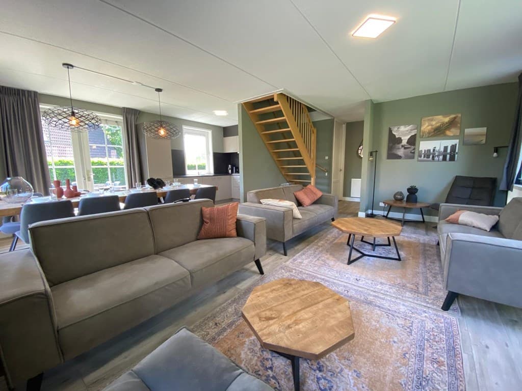 Ruimtelijk woonkamer met comfortabele zithoek, houten tafel, trap naar boven en uitzicht op de eetruimte en tuin