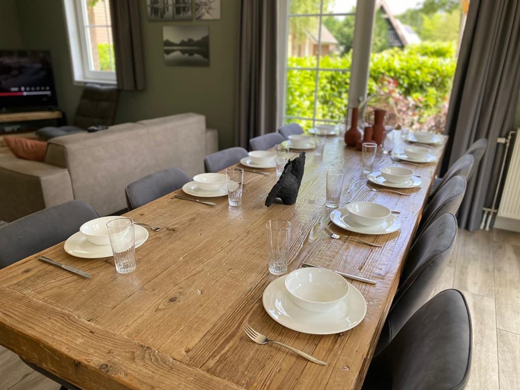 Eettafel met gedekte plaatsen en glazen, uitzicht op groen door openslaande deuren.