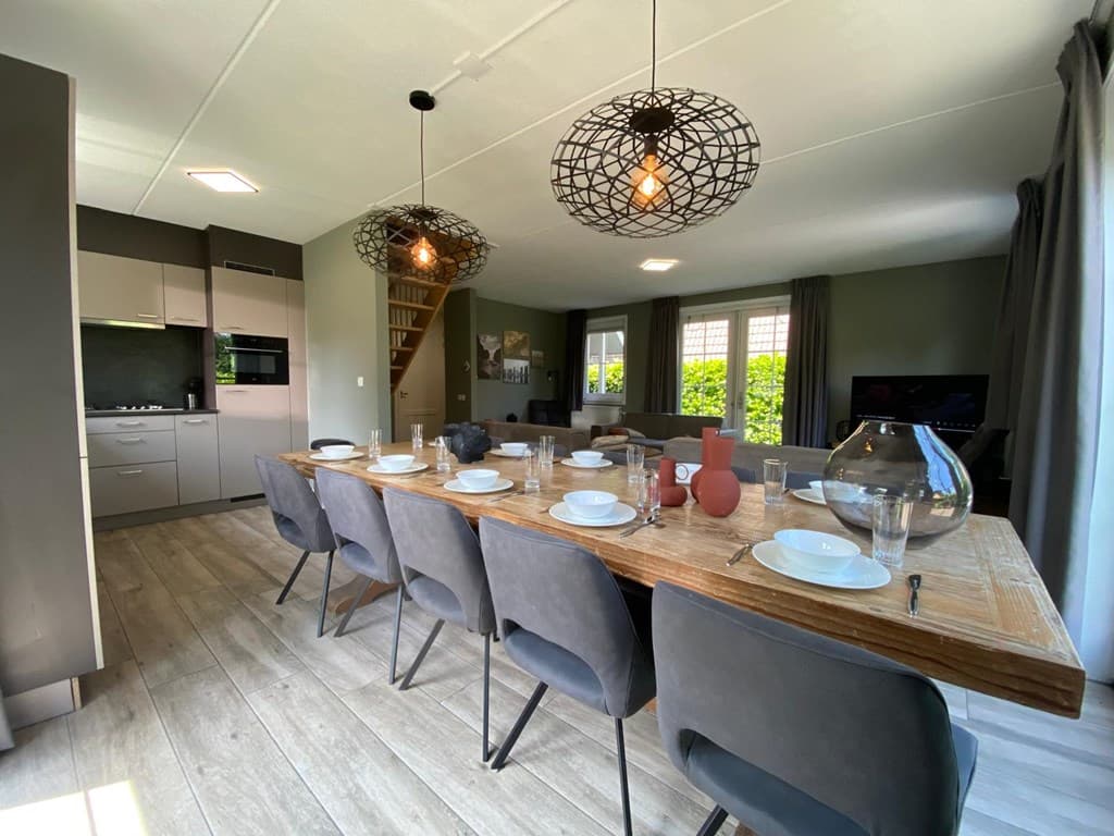 Eetkamerset met houten tafel en zwarte stoelen, keuken en woonkamer zichtbaar met moderne lampen en grote ramen
