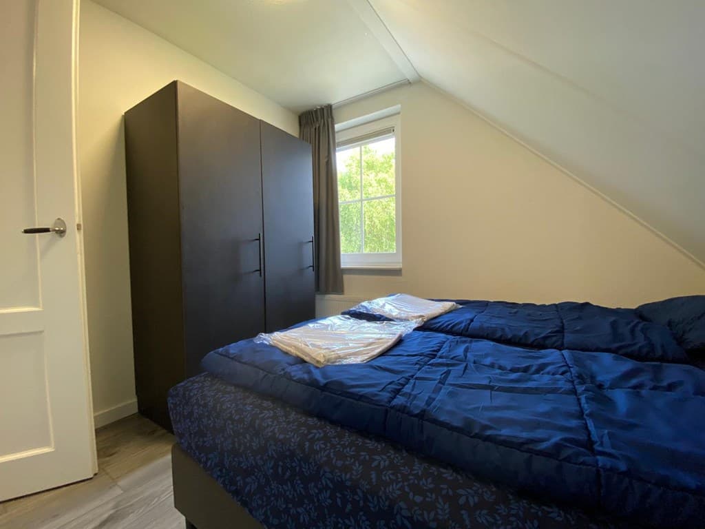 Slaapkamer met een bed, een kast en een raam met uitzicht op de natuur.