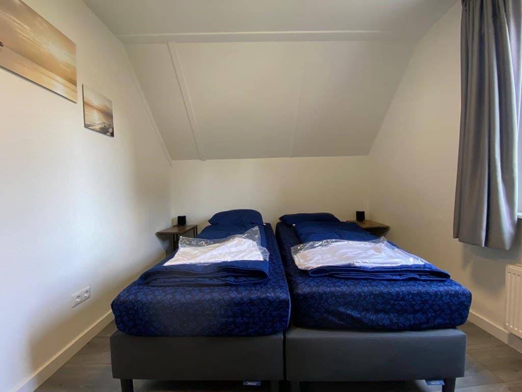 Slaapkamer met twee aparte bedden, nachtkastjes en een raam met een gordijn.