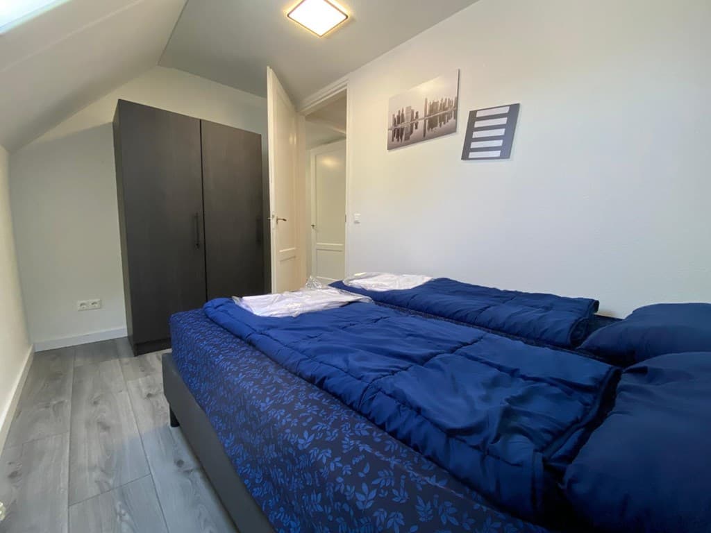 Slaapkamer met twee enkele bedden, kast en toegang tot een deur naar een andere ruimte.