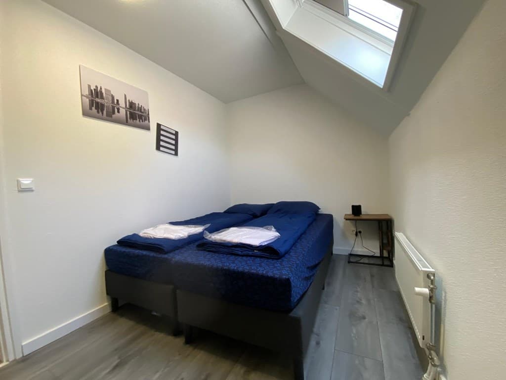 Slaapkamer met twee eenpersoonsbedden, bureau en raam in een lichte ruimte met witte muren