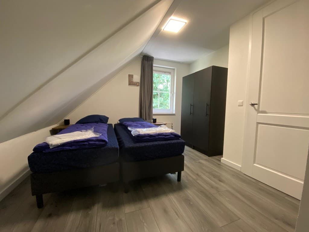 Slaapkamer met twee éénpersoonsbedden, een kast en een raam met uitzicht op de tuin.