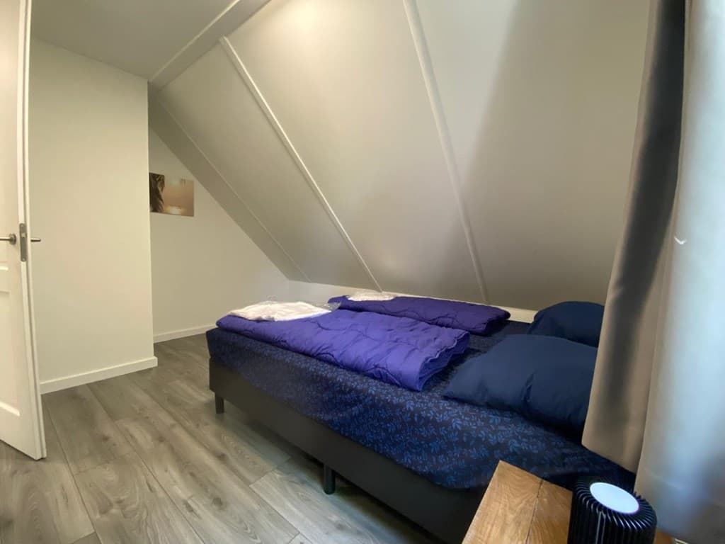Slaapkamer met schuin dak, twee aparte bedden en een houten nachtkastje met lampje.