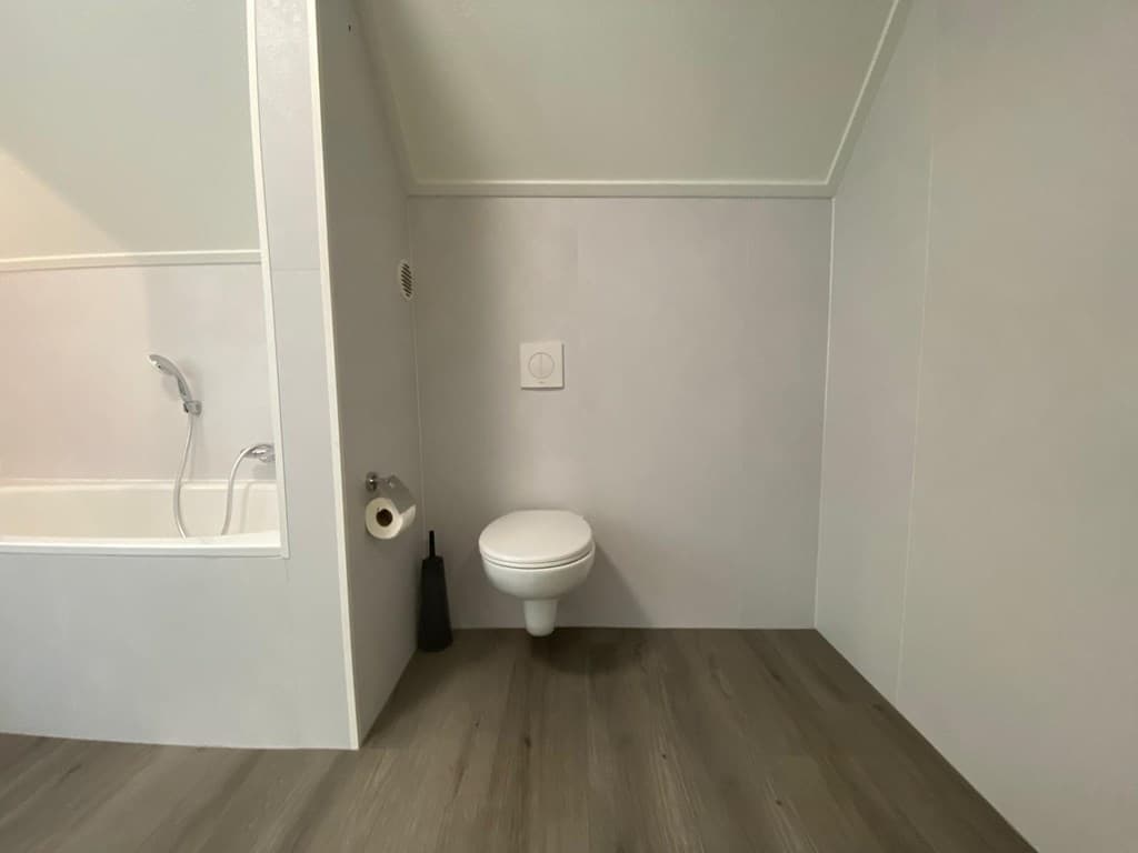 Lichte badruimte met een ligbad, wandtoilet en moderne afwerking op een houten vloer