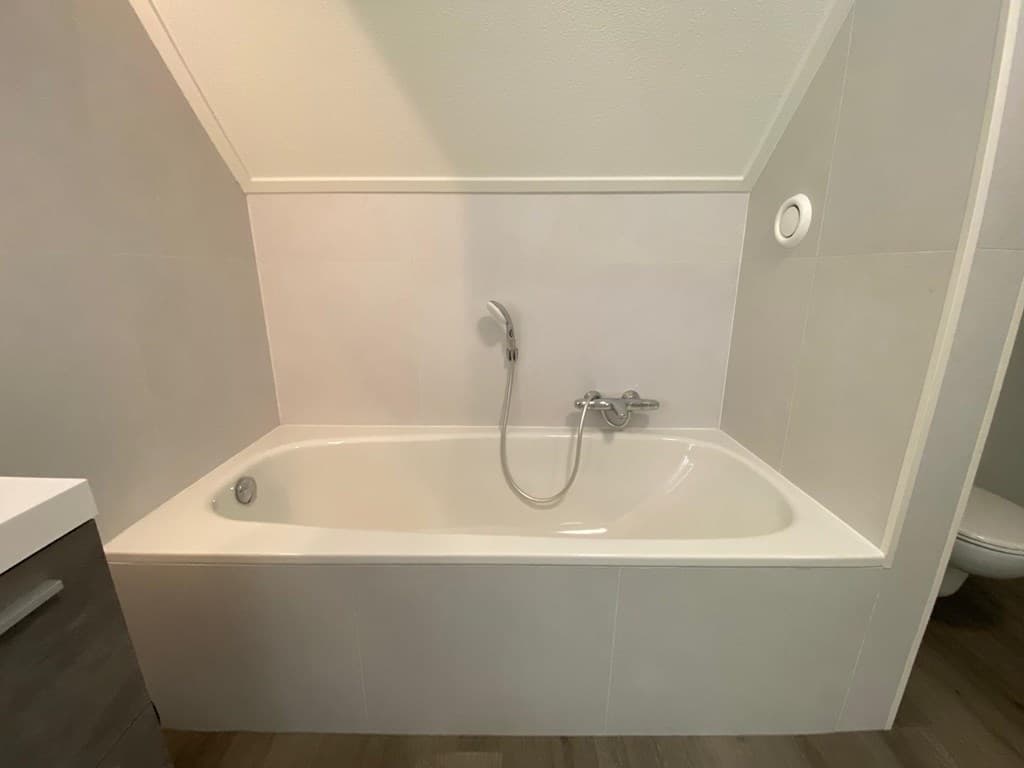 Badkamer met een vrijstaande badkuip, een mengkraan en een neutrale betegeling op de wanden en vloer