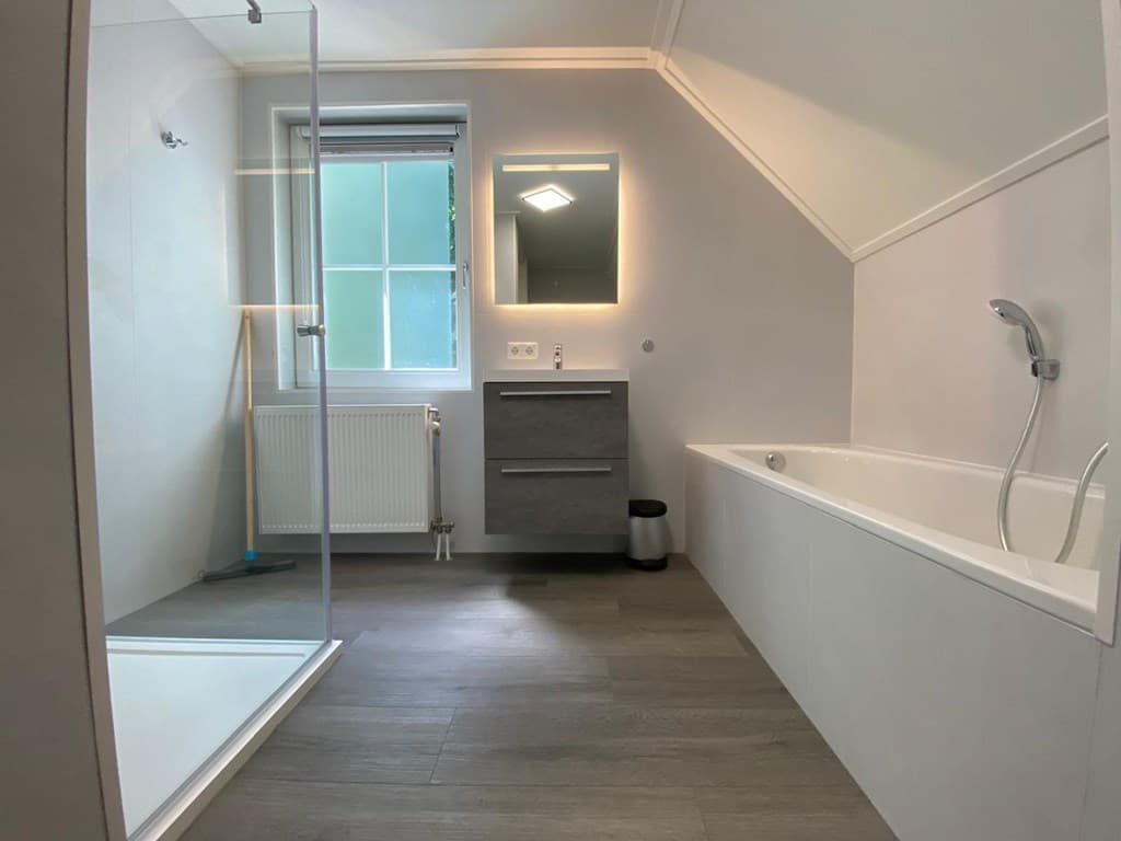 Ruime badkamer met een bad, inloopdouche, wastafel met spiegel en een raam voor natuurlijk licht