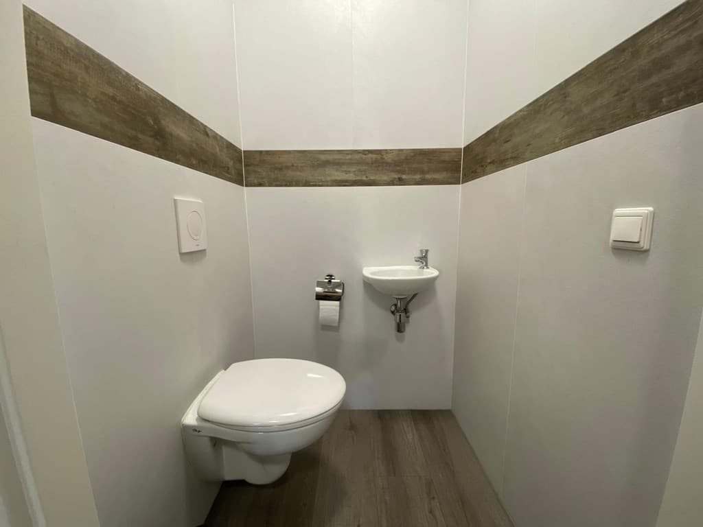 Toilet met wandtegels en een houten accentlijn, voorzien van een wc en een fonteintje tegen de muur