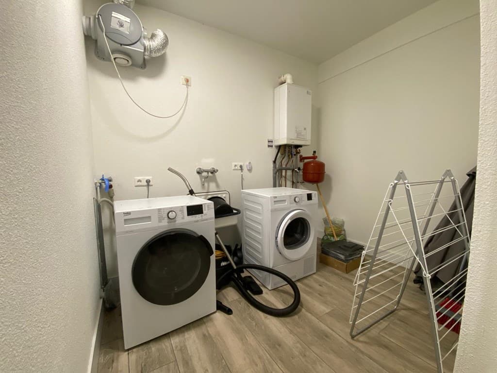 Wit wasruimte met wasmachines, droger, afvoerpunt en handdoekenrek aan de muur.