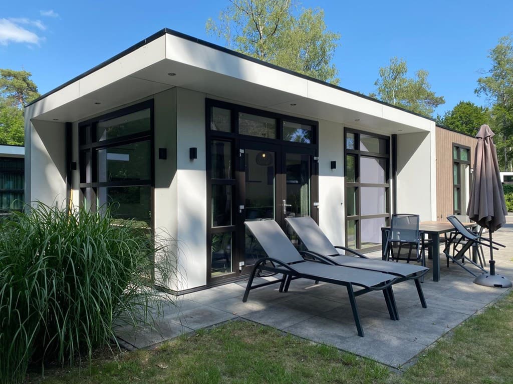 Moderne vakantiewoning met grote ramen, ligbedden en een terras, omgeven door groen op Recreatiepark Beekbergen