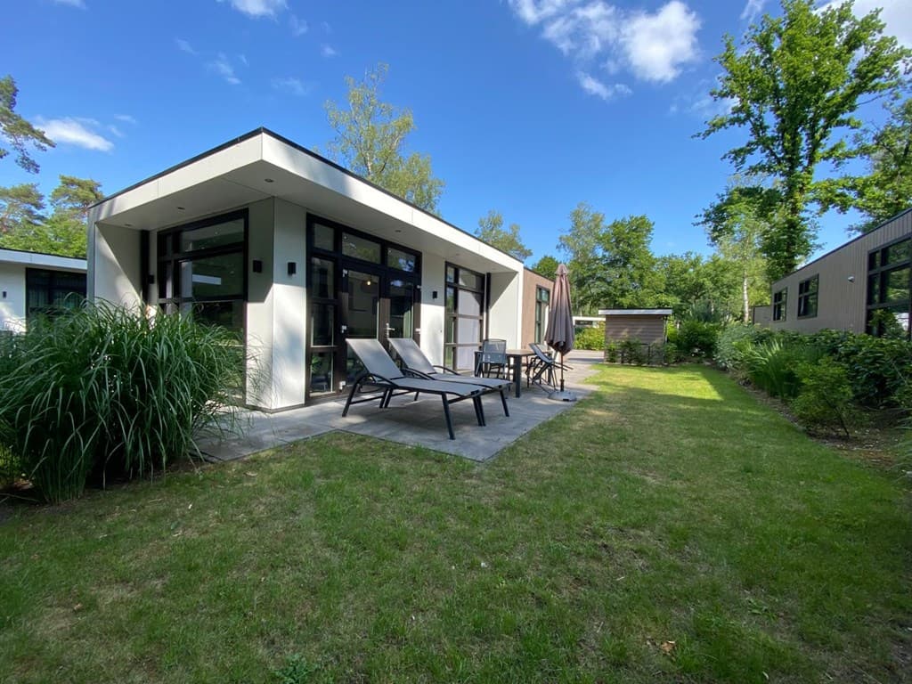 Moderne vakantiewoning met terras en ligstoelen, omringd door groene tuin en bomen