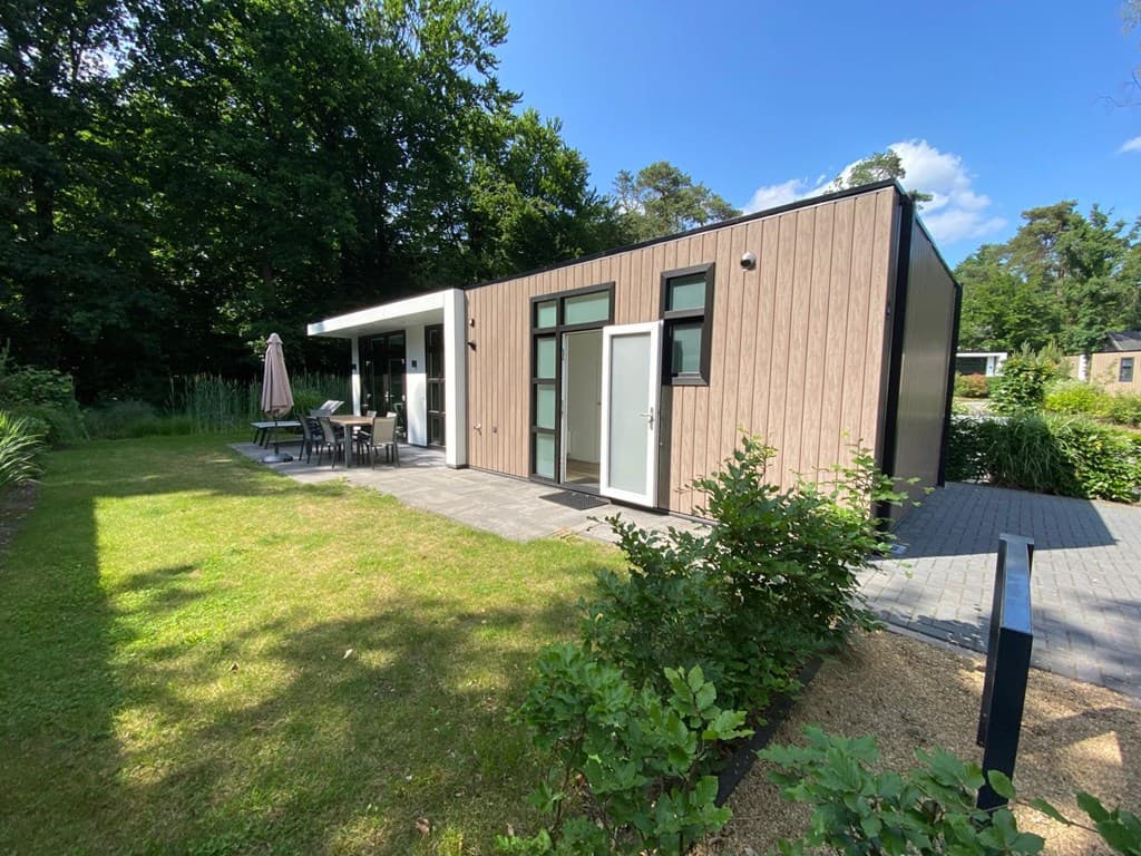 Moderne vakantiewoning met lichte gevel, terras en tuinmeubelen, omringd door groen in een parkachtige omgeving