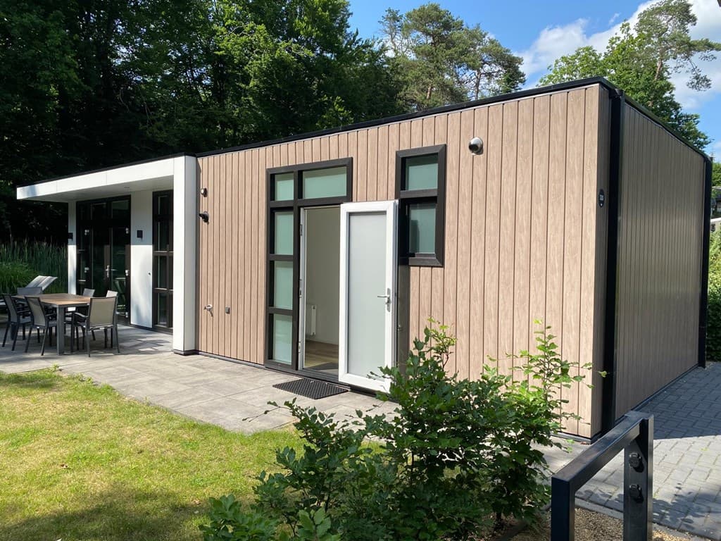 Moderne vakantiewoning met houten gevel en een betegeld terras, omgeven door groen en een tuinset buiten.