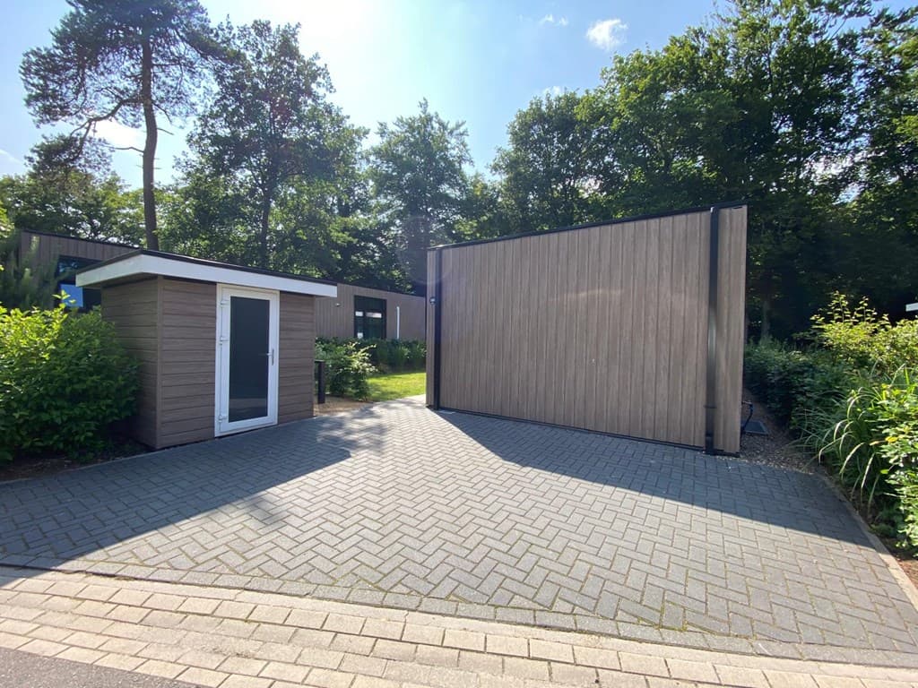 Moderne vakantiewoning met houten gevel en oprit, omgeven door groen en bomen.