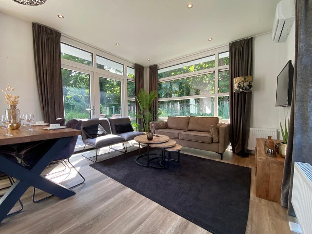Moderne woonkamer met grote ramen, comfortabele banken, een eettafel en houten decoraties in een vakantiehuis.