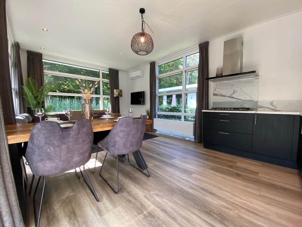 Eetkamer met een grote houten tafel en paarse stoelen, uitzicht op het buitengebied door grote ramen