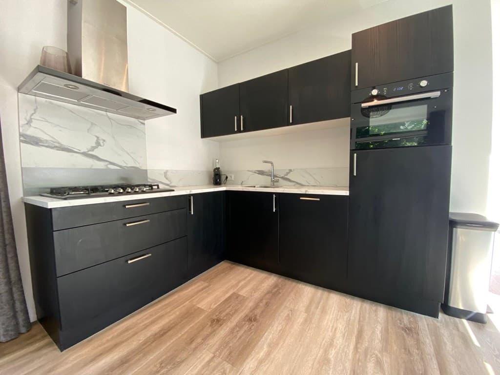 Moderne zwarte keuken met marmeren werkblad, gasfornuis en inbouwoven in vakantiehuis.