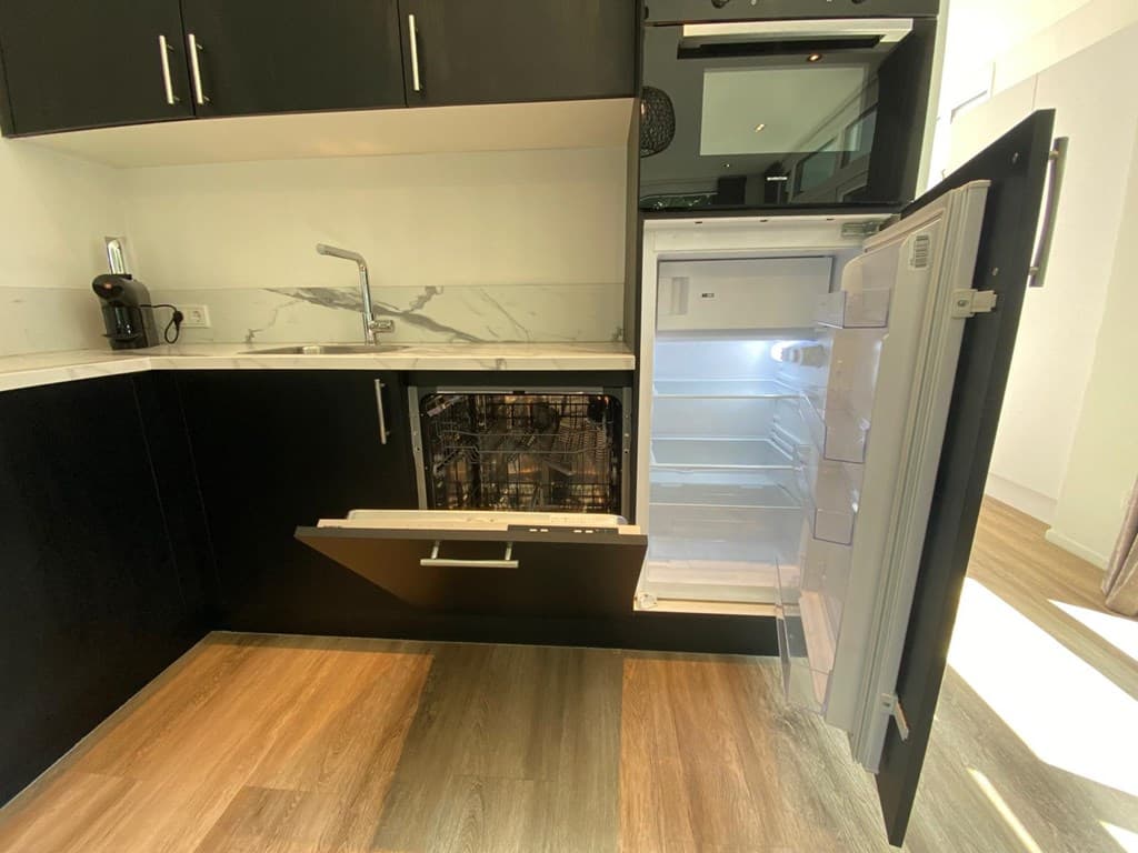 Moderne keuken met zwarte kastjes, openstaande vaatwasser en koelkast met een lichte binnenkant